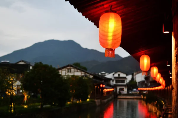 Night view photo of a traditional Chinese style corridor, with traditional Chinese lanterns hanging under the eaves, forming a reflection in the river, Zhejiang Province, China