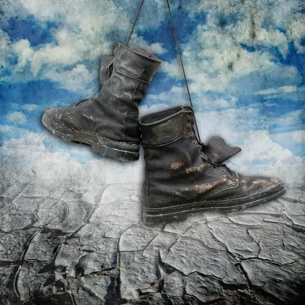 Botas militares viejas y sucias sobre fondo grunge con nubes y tierra de sequía — Foto de Stock