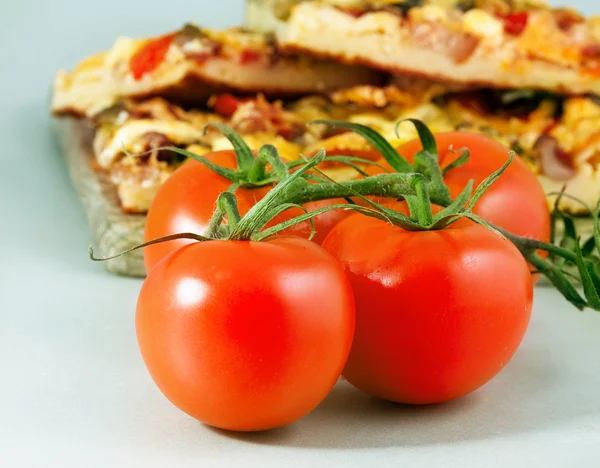 Pomodori con pizza sullo sfondo — Foto Stock