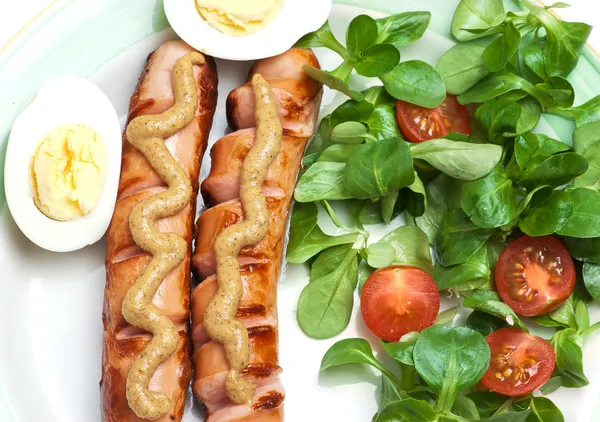 Sausages on the grill with mustard, egg, salad and tomatoes — Stock Photo, Image