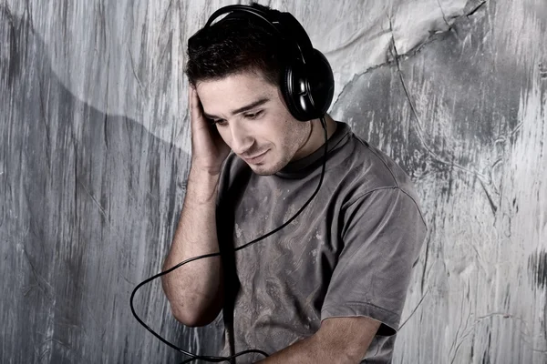 Retrato de un joven guapo escuchando música contra una pared grunge — Foto de Stock