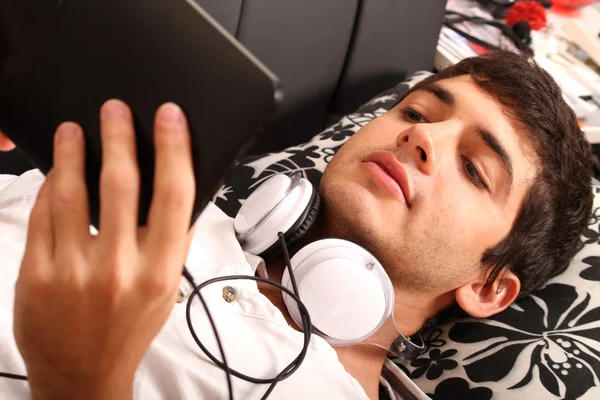 Jeune homme avec une tablette PC et écouteurs sur le canapé — Photo