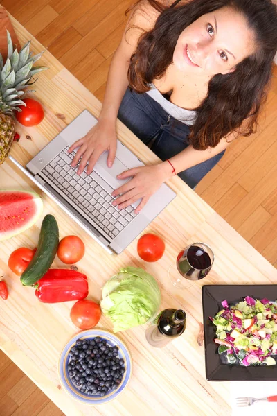 Kvinna som använder en bärbar dator medan matlagning — Stockfoto