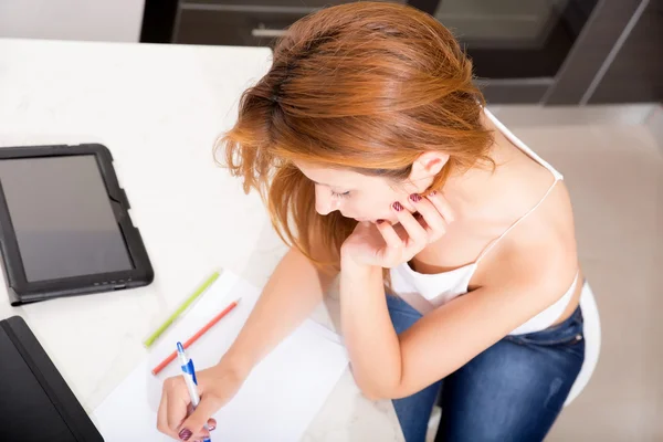 Roodharige meisje schrijven in keuken — Stockfoto