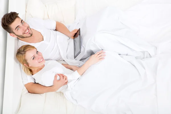 Jeune couple avec une tablette PC au lit — Photo