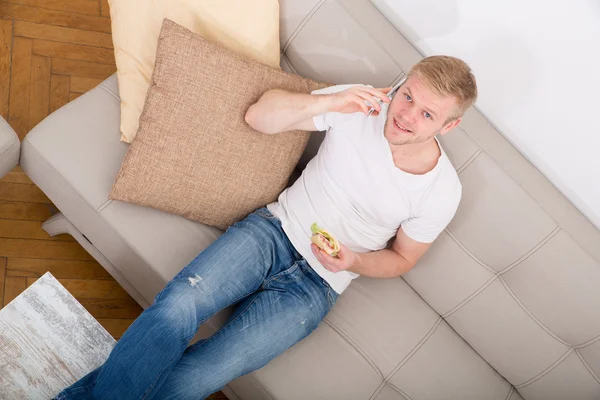 Joven con un sándwich en el sofá — Foto de Stock