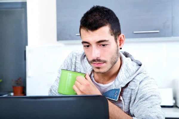Jeune homme avec ordinateur portable dans la cuisine — Photo