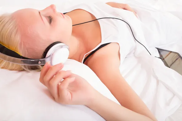 Blond meisje liggend in bed luisteren naar muziek — Stockfoto