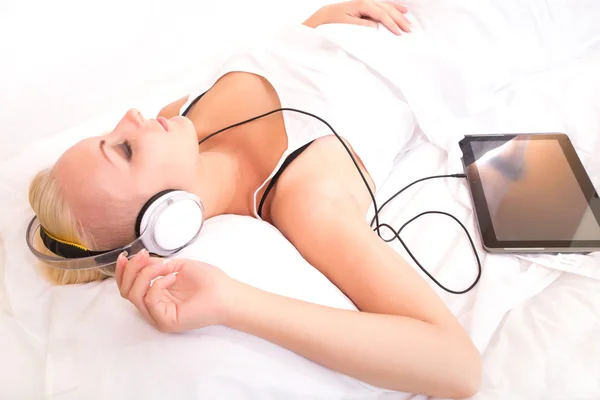 Blonďatá holka ležící v posteli poslouchá hudbu — Stock fotografie