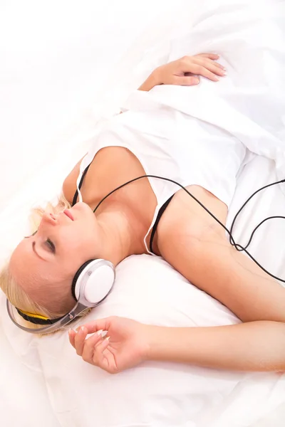 Blondynka, leżąc w łóżku słuchając muzyki — Zdjęcie stockowe