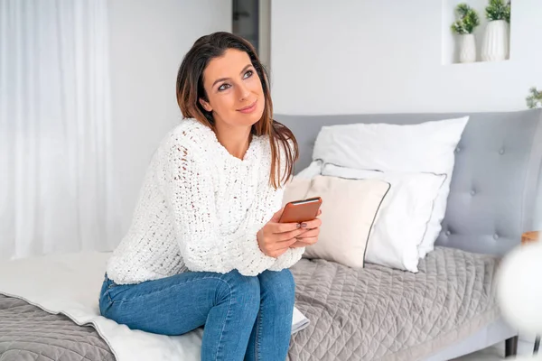 Une femme réfléchie avec son téléphone assis sur le lit Photos De Stock Libres De Droits