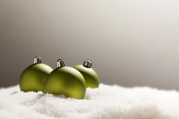 Grüne Christbaumkugeln auf Schnee vor grauem Hintergrund — Stockfoto