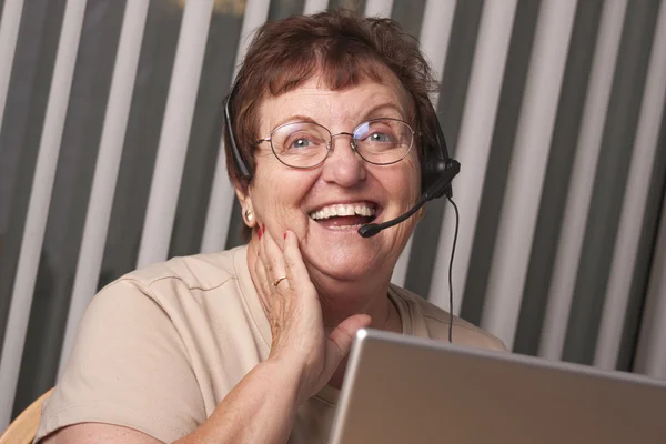 Mulher adulta sênior sorridente com fone de ouvido e monitor telefônicos — Fotografia de Stock