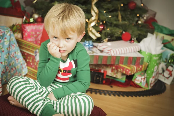 Niño gruñón sentado cerca del árbol de Navidad — Foto de Stock