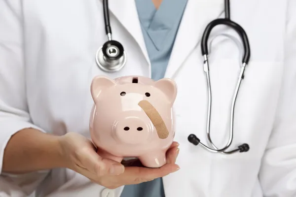 Médico segurando Piggy Bank com bandagem no rosto — Fotografia de Stock