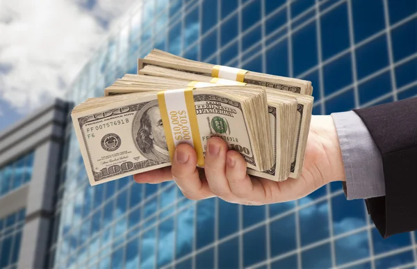 Mão masculina segurando pilha de dinheiro com edifício corporativo — Fotografia de Stock