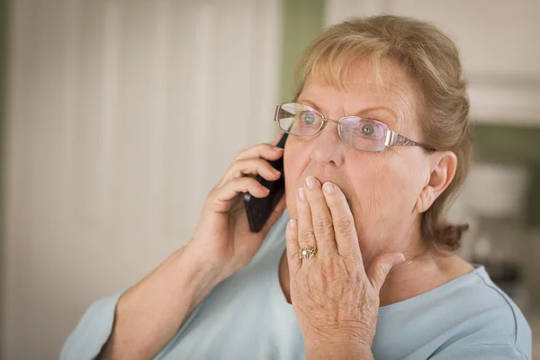 Mujer adulta mayor conmocionada en el teléfono celular en la cocina — Foto de Stock