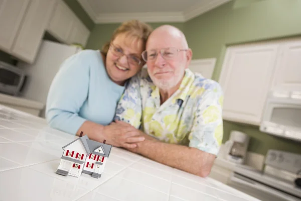 Senioren-Ehepaar blickt über kleines Musterhaus auf dem Tresen — Stockfoto