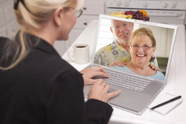 Mujer en la cocina usando el ordenador portátil - En línea con la pareja de ancianos —  Fotos de Stock
