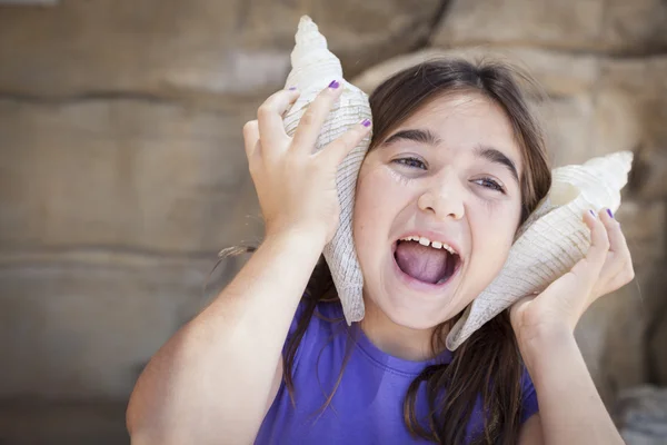 Ung flicka som leker med stora snäckskal mot hennes öron — Stockfoto