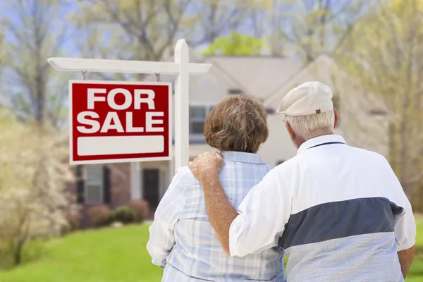 Glückliches Seniorenpaar vor Verkaufsschild und Haus — Stockfoto