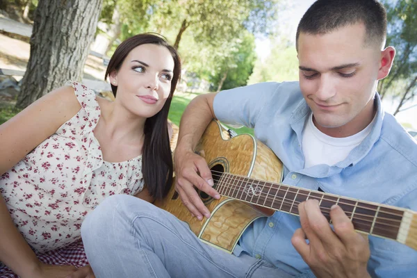 Casal de corrida mista no parque tocando guitarra e canto — Fotografia de Stock