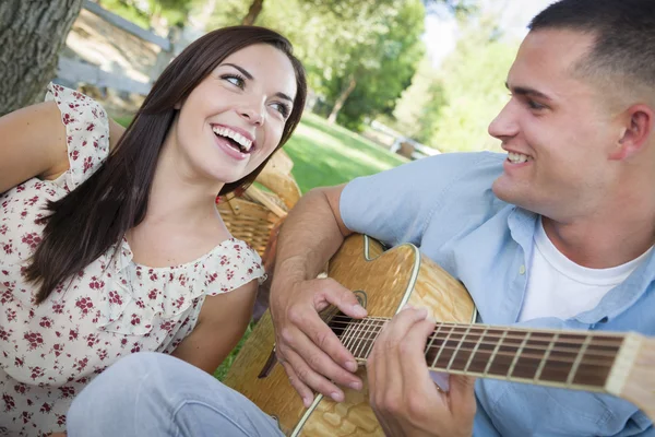 Casal de corrida mista no parque tocando guitarra e canto — Fotografia de Stock