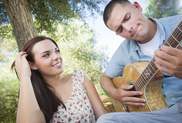 Смешанная расовая пара в парке играет на гитаре и поет — стоковое фото