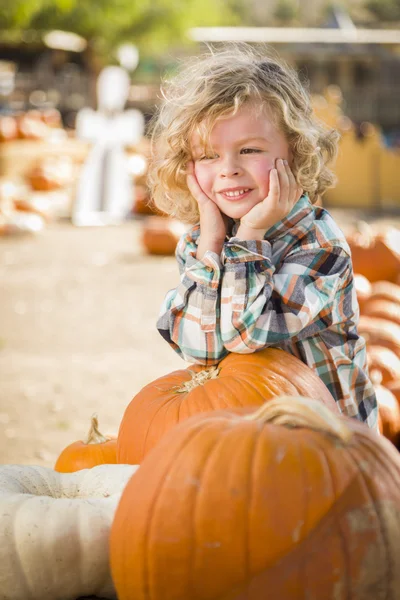 Kleine jongen glimlacht terwijl leunend op pompoen op pompoen patch — Stockfoto