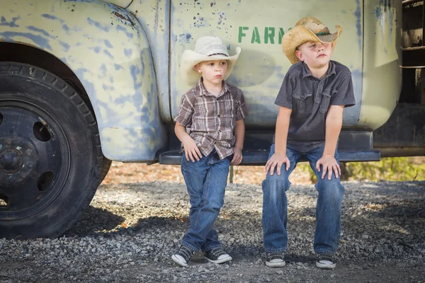Dwóch młodych chłopców kapelusze kowbojskie, opierając się na sobie starodawny samochódantika kamyon karşı yaslanmış kovboy şapkası giyen iki genç erkek — Stok fotoğraf