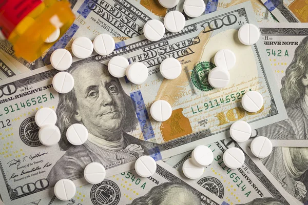 Лекарственные таблетки, разбросанные по недавно разработанным 100 долларовым счетам — стоковое фото