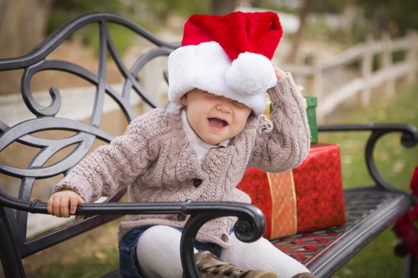 Маленький ребенок в Санта-Шляпе сидит с рождественскими подарками на улице — стоковое фото