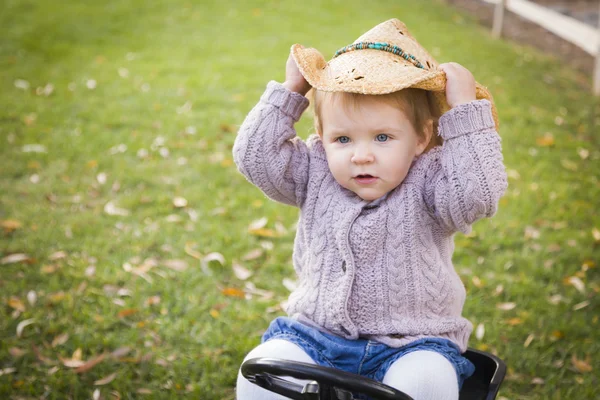 Kovboy şapkası giyen ve dışında oyuncak traktör üzerinde oyun toddler — Stok fotoğraf