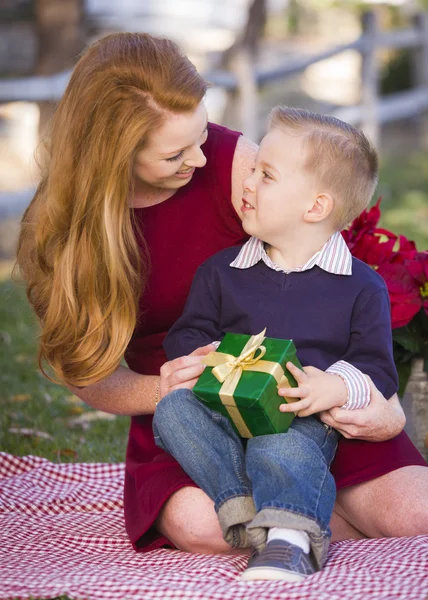 Ung pojke håller julklapp med sin mamma i park — Stockfoto