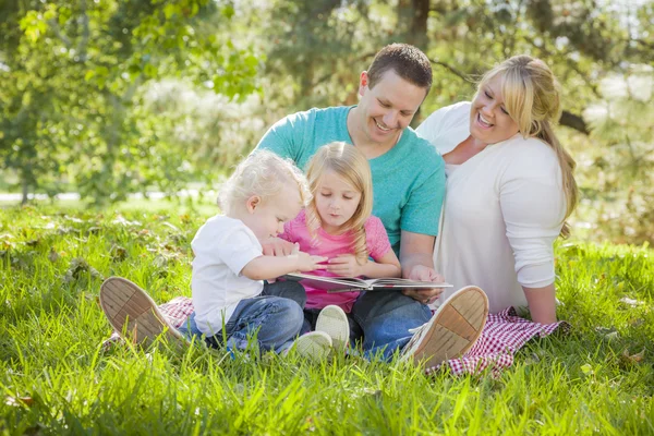 Mladá rodina se těší, čtení knihy v parku — Stock fotografie
