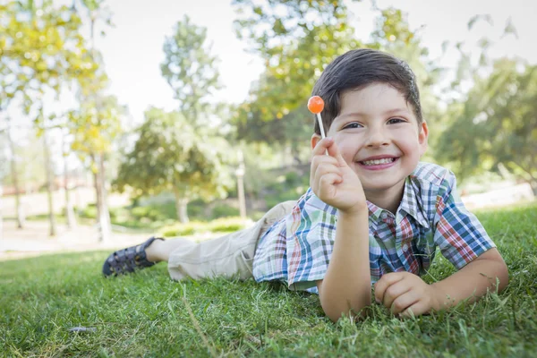 Jonge jongen genieten van zijn lollipop buitenshuis opleggen gras — Stockfoto