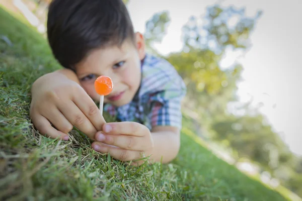 Ung pojke njuter av hans lollipop om utomhus på gräs — Stockfoto