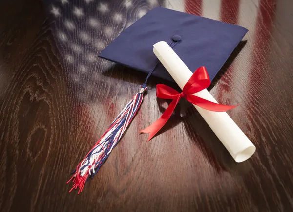 Examen mössa och dipoma på bordet med amerikanska flaggan reflektion — Stockfoto