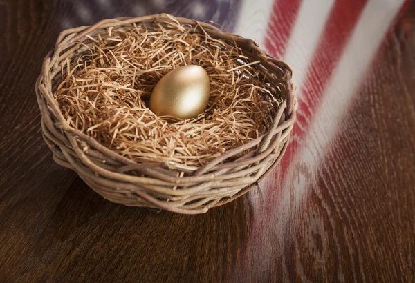 Золотое яйцо в гнезде с отражением американского флага на столе — стоковое фото