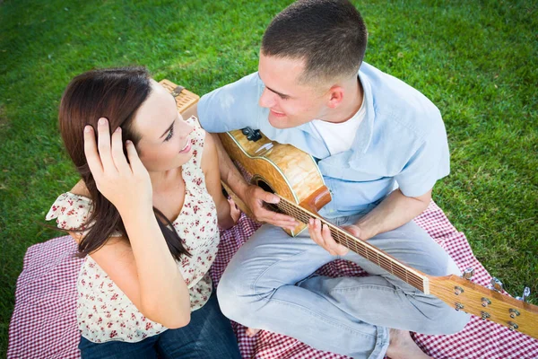 公園で彼のガールフレンドのための若い大人の男演奏ギター — ストック写真