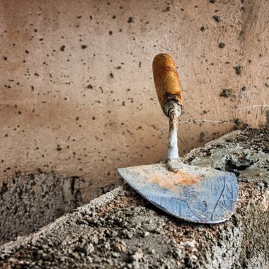 Dirty trowel above a concrete wall