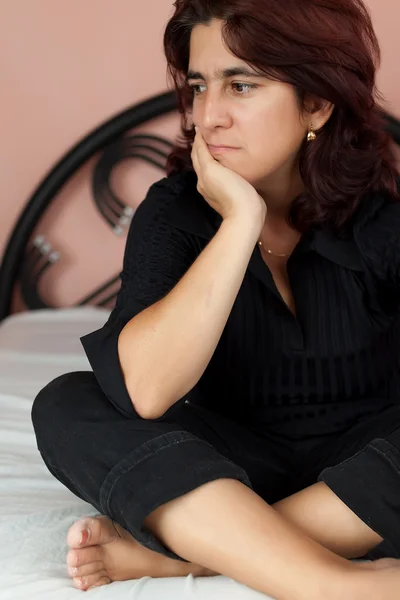 Mulher sentada em sua cama com uma expressão preocupada — Fotografia de Stock