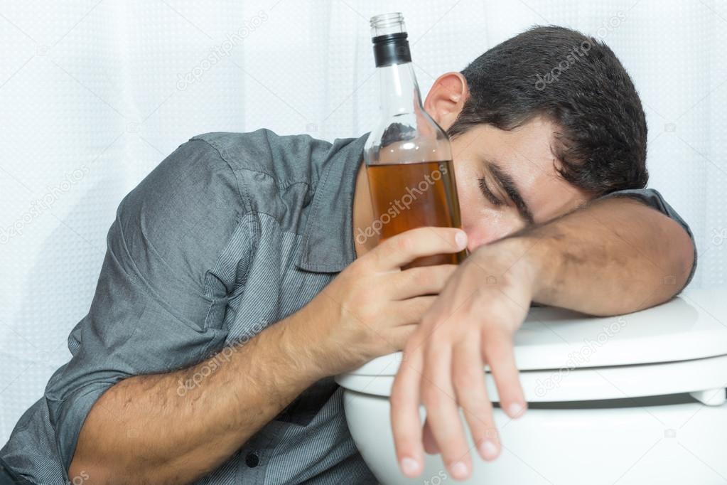 Drunk man sleeping on the toilet and holding a bottle