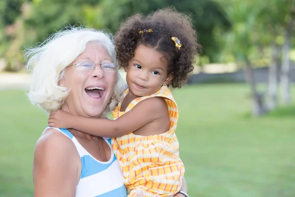 Caucasian grandma carrying her hispanic granddaughter — Stock Photo, Image