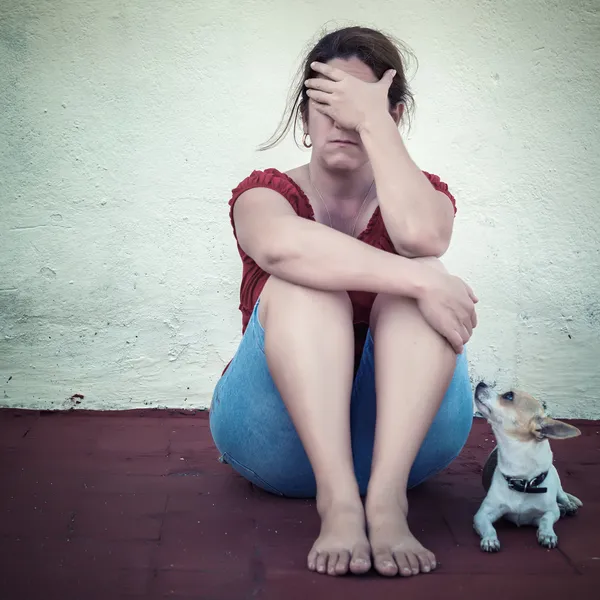Сумна жінка плаче з маленьким собакою поруч з нею — стокове фото