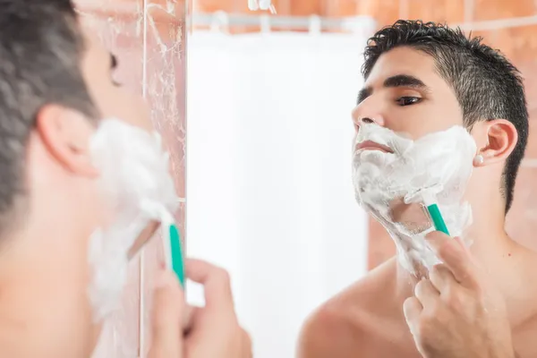Shirtless hispanic man shaving in front of a mirror — Stock Photo, Image