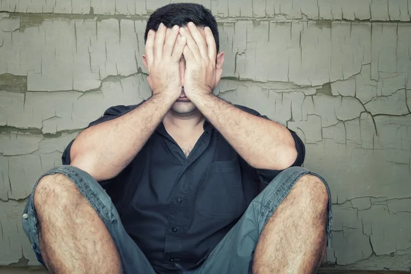 Depressieve jonge man zittend op de vloer en die betrekking hebben op zijn gezicht — Stockfoto