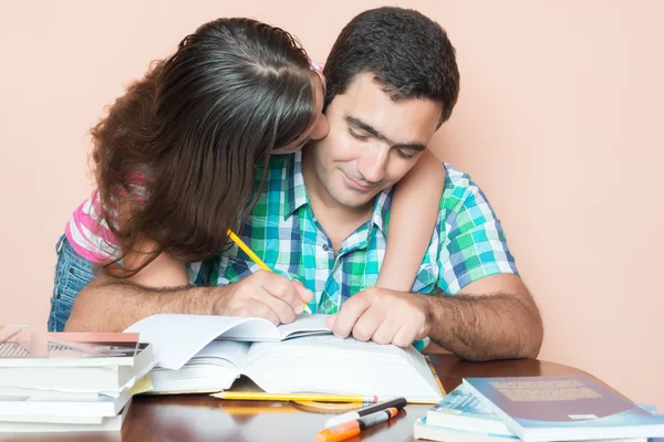 Jovem estudando com sua filha beijando-o — Fotografia de Stock