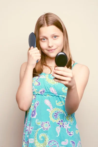 Adolescente chica sosteniendo cepillo de pelo y mirando al espejo — Foto de Stock