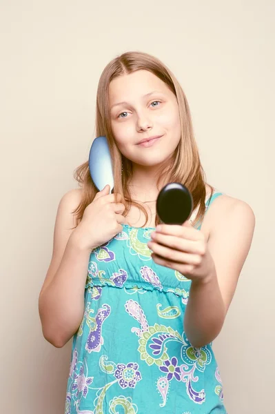 Ragazza adolescente che tiene la spazzola per capelli e guarda lo specchio — Foto Stock